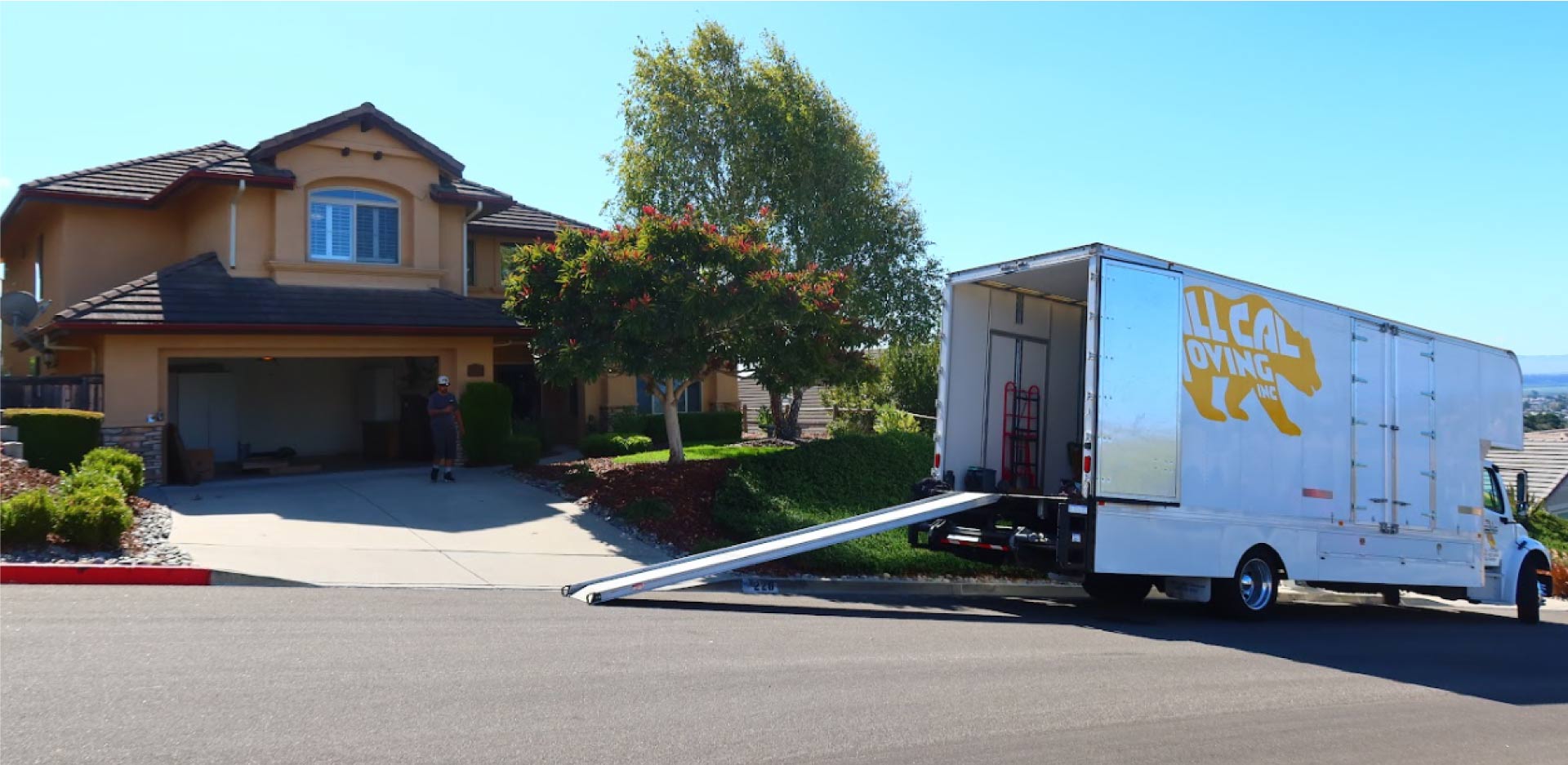 All Cal Moving truck with a loading ramp extended outside a two-story house in Tulare County while a professional mover prepares to load furniture